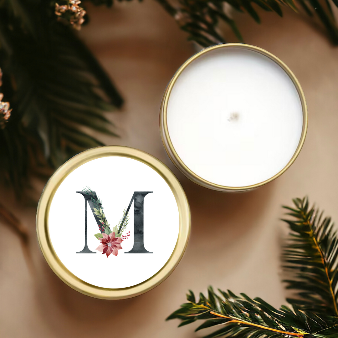 A gold tin candle with a holiday themed initial M.