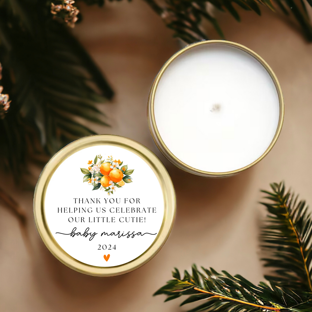 A gold tin candle with a personalized label and oranges.