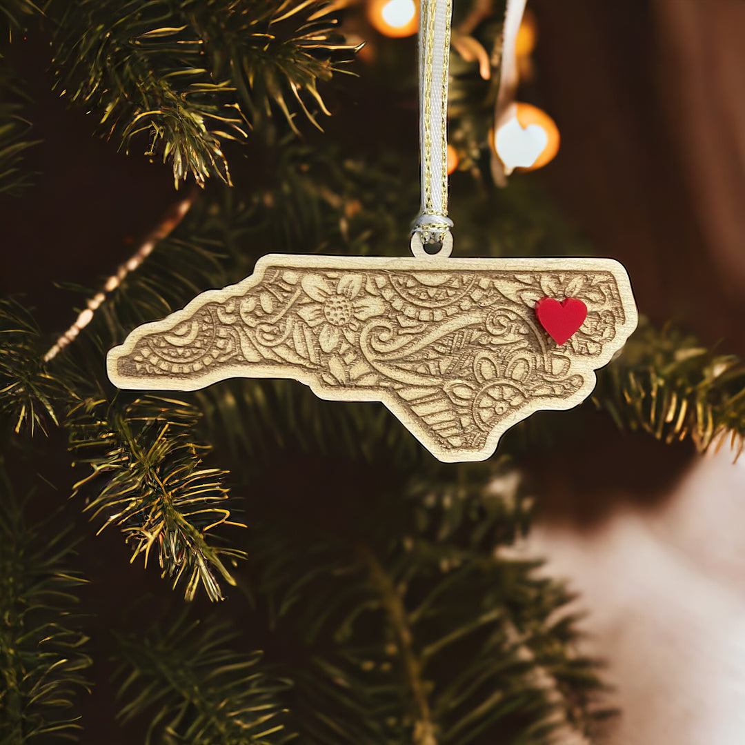 Wooden New Carolina ornament with white and gold ribbon and red heart.