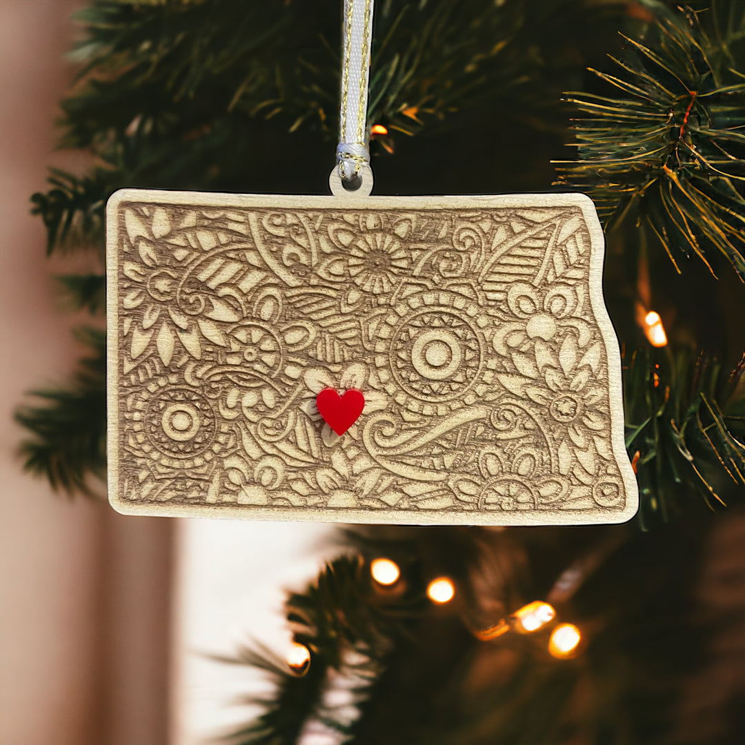 Wooden New Dakota ornament with white and gold ribbon and red heart.