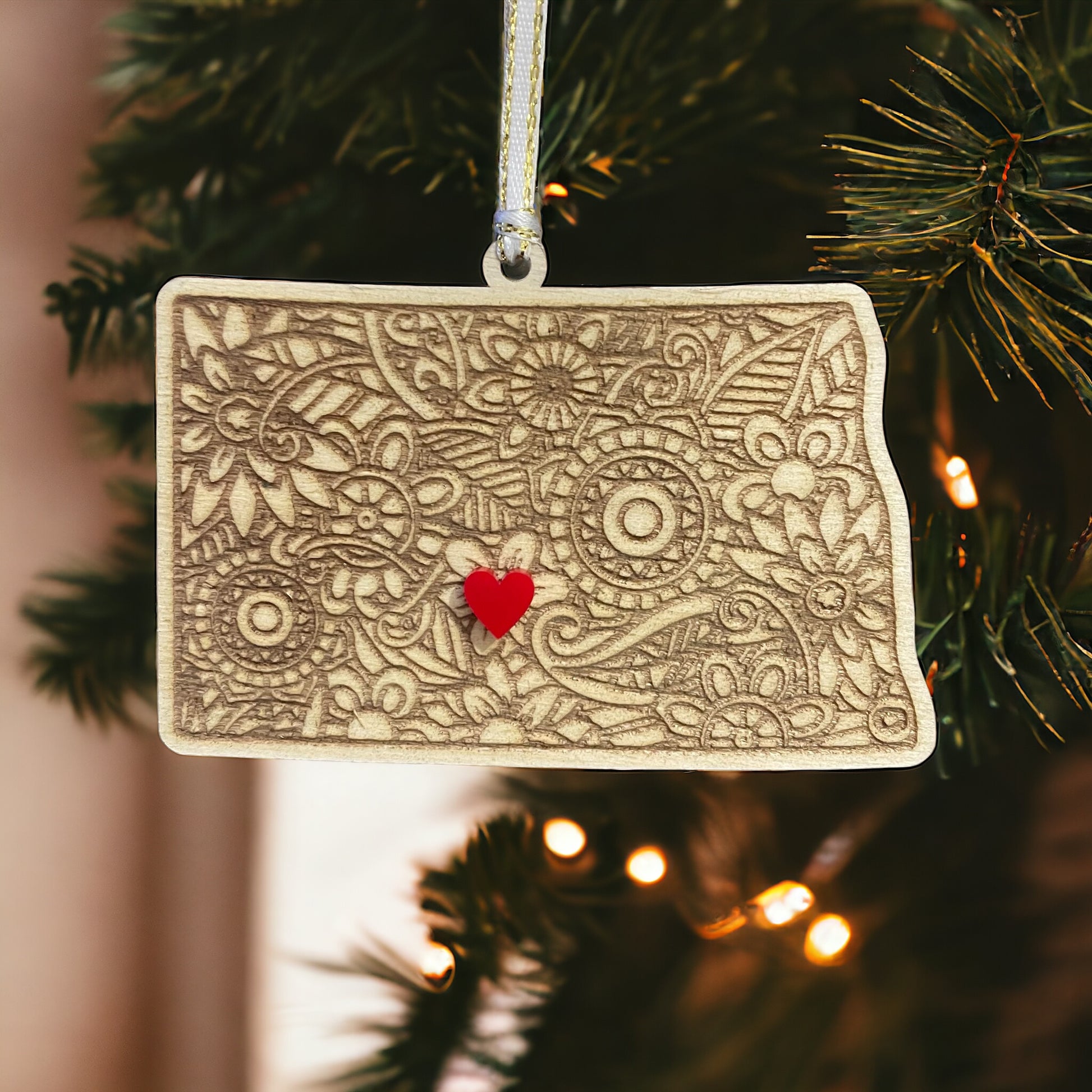 Wooden New Dakota ornament with white and gold ribbon and red heart.