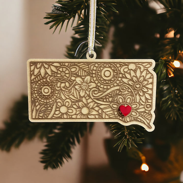 Wooden South Dakota ornament with white and gold ribbon and red heart.