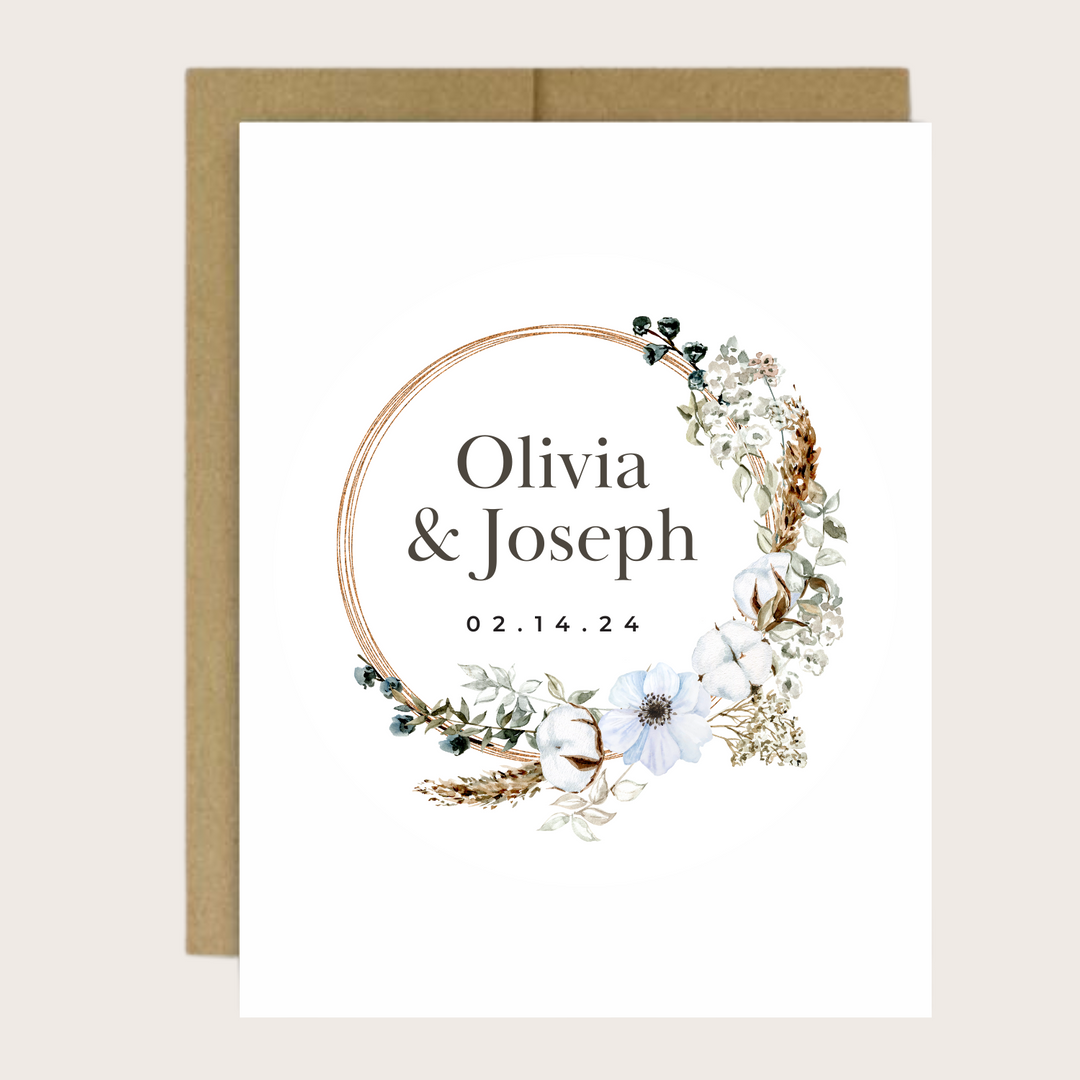 A gold floral wreath greeting card with a couple's name and event date.