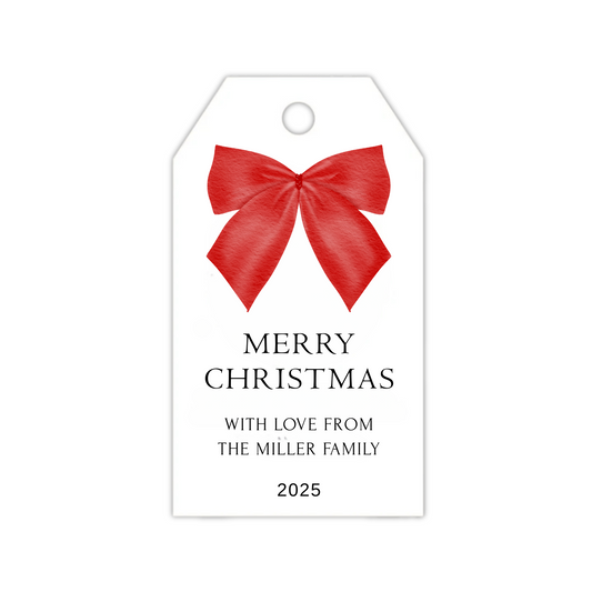 A red Christmas bow gift tag with holiday sentiment and personalized name and year.