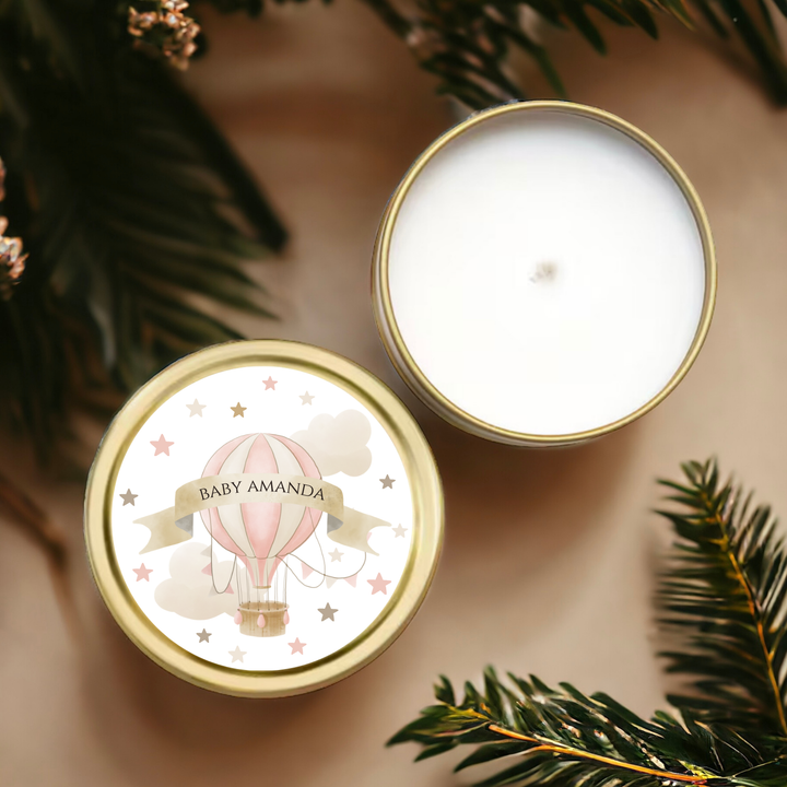 A gold tin candle with a label with a pink hot air balloon and pink and brown stars