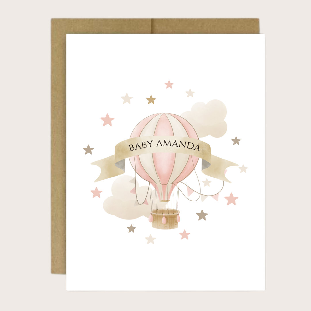 A greeting card with a pink hot air balloon, clouds and stars with a banner and a baby's name.