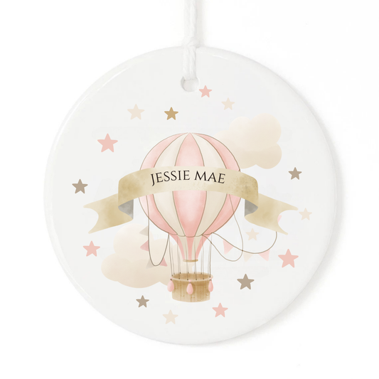 A white ornament with a pink hot air balloon personalized with a name.