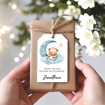 A small gift box with a gift tag with blue and yellow moon and stars and a sleeping teddy bear.