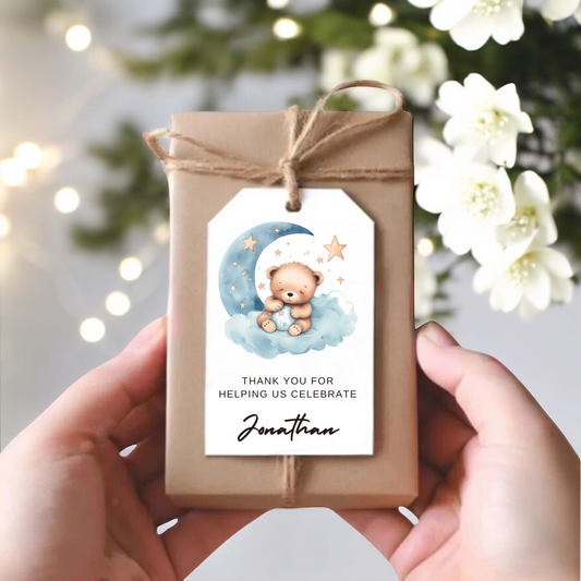 A small gift box with a gift tag with blue and yellow moon and stars and a sleeping teddy bear.